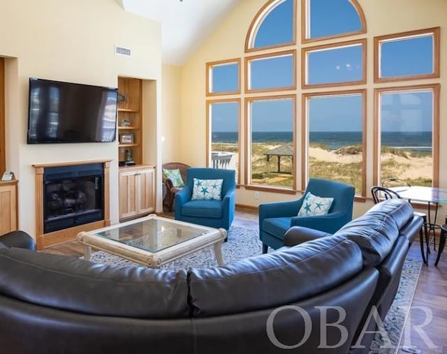 living room featuring high vaulted ceiling, a glass covered fireplace, wood finished floors, and visible vents