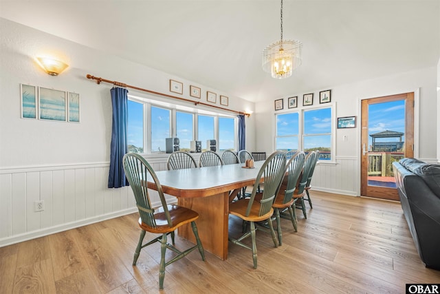 dining room with a chandelier, lofted ceiling, a wainscoted wall, and light wood finished floors