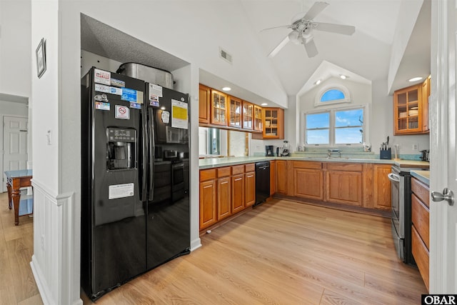 kitchen featuring glass insert cabinets, brown cabinets, light countertops, and black appliances