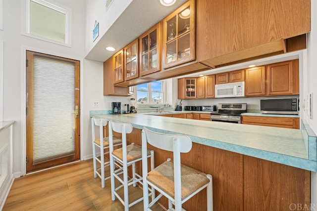 kitchen featuring a breakfast bar area, stainless steel appliances, a peninsula, light countertops, and glass insert cabinets