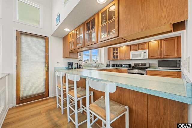 4939 S Virginia Dare Trl Lot 4, Nags Head, NC 27959 - kitchen with stainless steel appliances, a peninsula, light wood-style floors, glass insert cabinets, and brown cabinetry