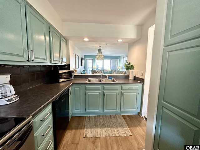 kitchen with black dishwasher, dark countertops, a sink, and light wood-style flooring