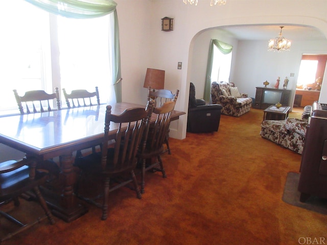 carpeted dining room with arched walkways, a chandelier, and a wealth of natural light