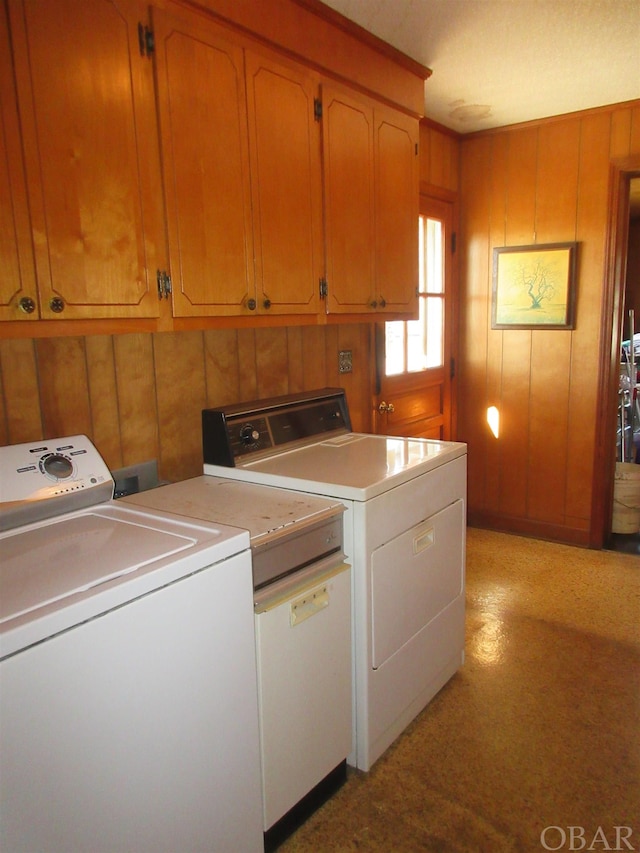 laundry area with washing machine and dryer, cabinet space, and wood walls