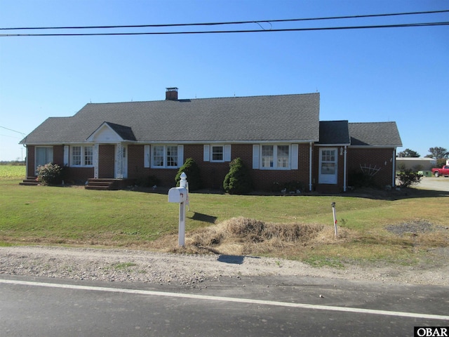 ranch-style home with brick siding, a shingled roof, a chimney, and a front yard