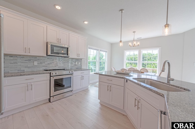 kitchen with tasteful backsplash, white cabinets, appliances with stainless steel finishes, light wood-style floors, and a sink