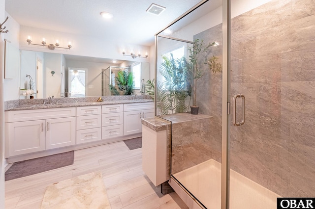 bathroom featuring double vanity, a shower stall, visible vents, and a sink