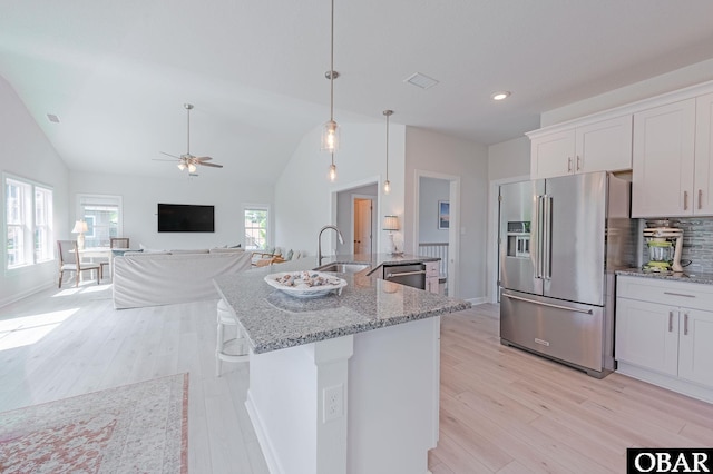 kitchen with light wood finished floors, white cabinets, light stone countertops, stainless steel appliances, and a sink