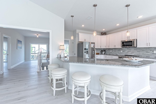 kitchen featuring light stone counters, stainless steel appliances, backsplash, white cabinetry, and a sink