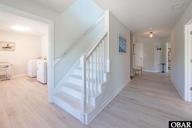 hall with light wood-type flooring, visible vents, stairway, and washing machine and clothes dryer