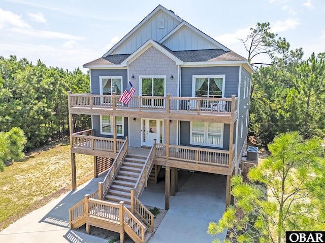 raised beach house with a shingled roof, board and batten siding, a carport, cooling unit, and stairs