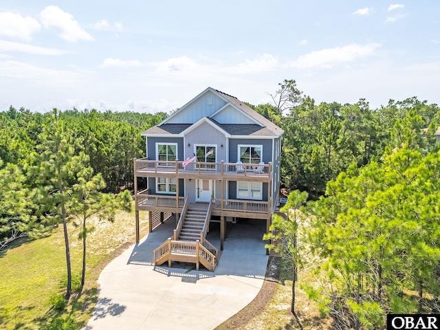 view of front of home featuring roof with shingles, concrete driveway, board and batten siding, a carport, and stairs