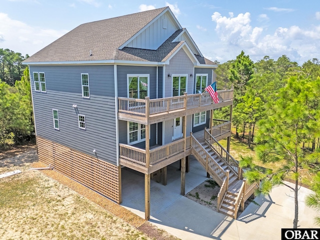 rear view of property with a deck, a shingled roof, stairs, concrete driveway, and board and batten siding