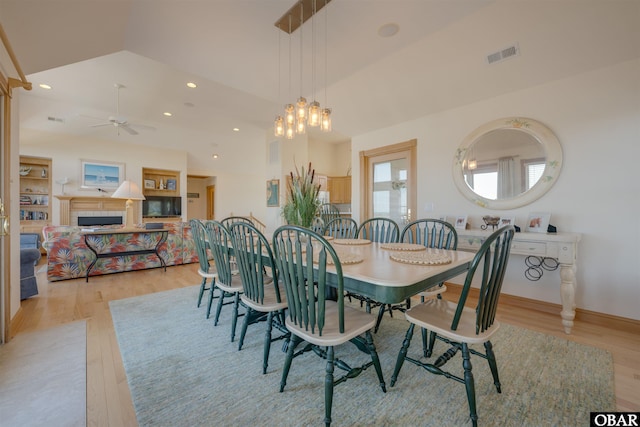 dining room featuring light wood-type flooring, ceiling fan with notable chandelier, lofted ceiling, and visible vents