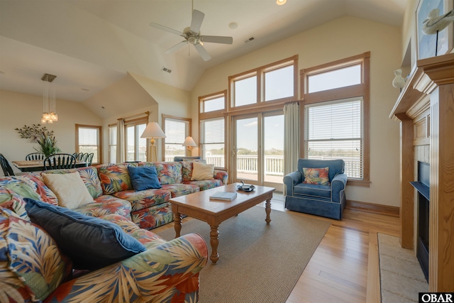 living area featuring light wood-type flooring, high vaulted ceiling, a fireplace, and a wealth of natural light