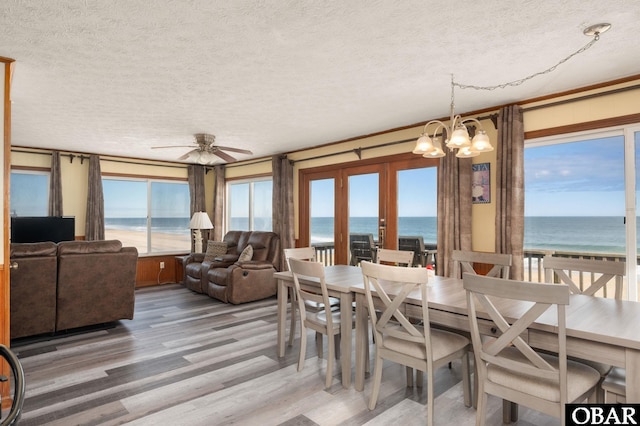 dining room with light wood-type flooring, a water view, a textured ceiling, and ceiling fan with notable chandelier