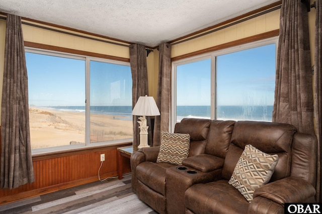 living area featuring a water view, a textured ceiling, wooden walls, and wood finished floors