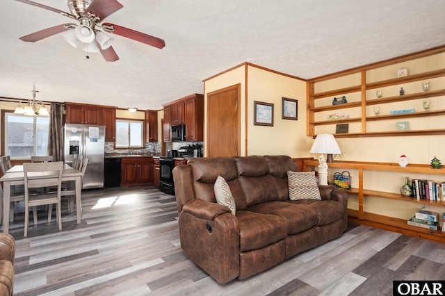 living area featuring light wood-style floors, ornamental molding, a textured ceiling, and ceiling fan with notable chandelier