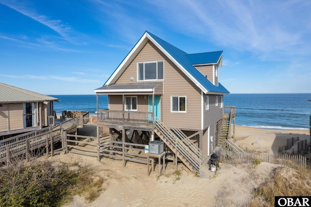 rear view of property featuring stairway, a water view, metal roof, and a beach view