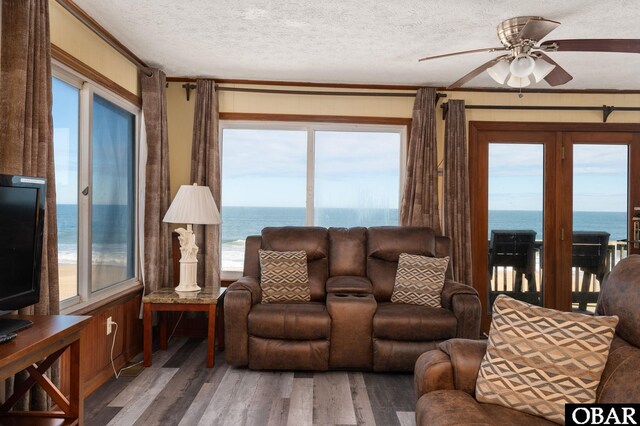 living room featuring a water view, ceiling fan, a textured ceiling, and wood finished floors