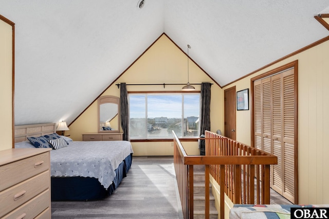 bedroom with lofted ceiling, light wood finished floors, ornamental molding, and a closet