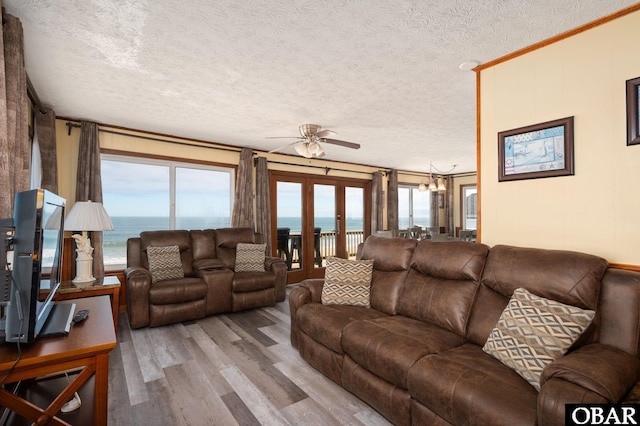 living area with wood finished floors, a water view, a textured ceiling, french doors, and ceiling fan with notable chandelier