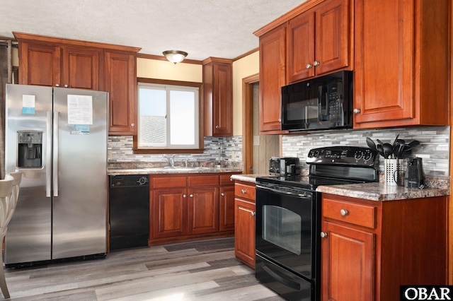 kitchen featuring brown cabinets, decorative backsplash, light wood-style floors, a sink, and black appliances