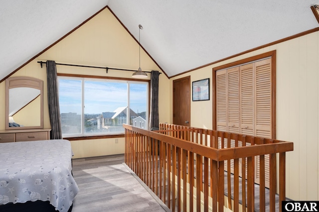 bedroom featuring ornamental molding, vaulted ceiling, wooden walls, and wood finished floors