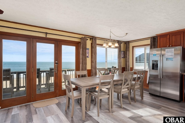 dining space with a textured ceiling, a water view, light wood-style flooring, and an inviting chandelier