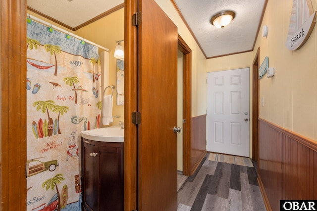 interior space with a textured ceiling, ornamental molding, a wainscoted wall, and vanity