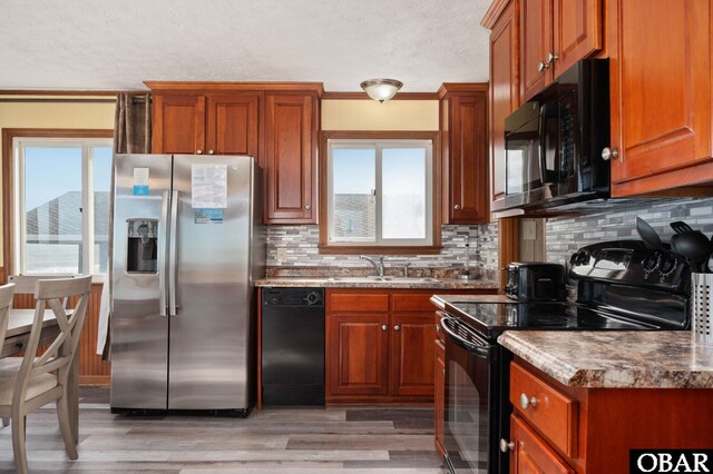 kitchen featuring light wood-style flooring, a sink, decorative backsplash, brown cabinets, and black appliances