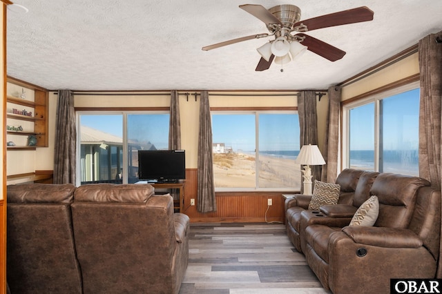 living area featuring a ceiling fan, a textured ceiling, wooden walls, and wood finished floors