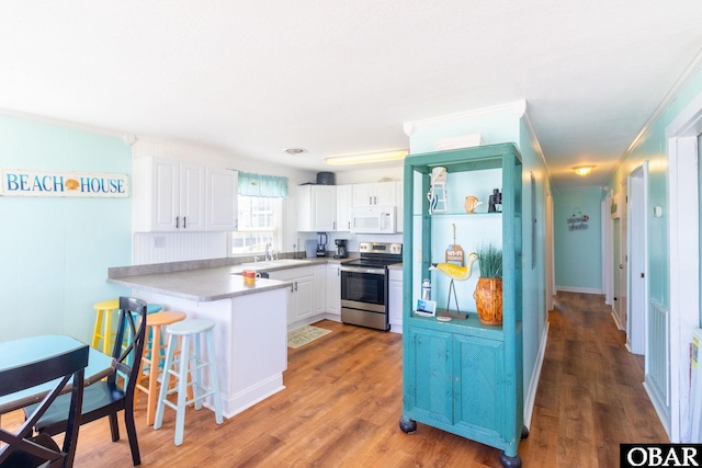 kitchen with white cabinets, white microwave, a peninsula, light countertops, and stainless steel range with electric cooktop