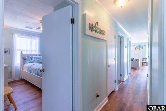 corridor with ornamental molding, visible vents, and wood finished floors