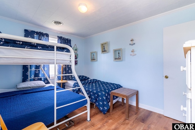 bedroom featuring baseboards, wood finished floors, visible vents, and crown molding