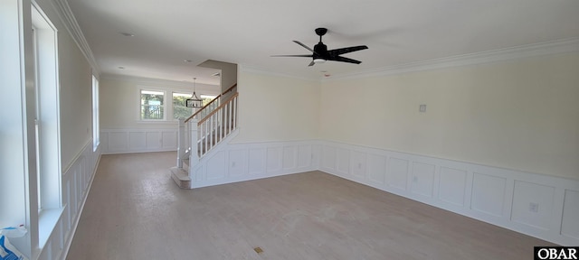 unfurnished room featuring stairway, a decorative wall, crown molding, and wainscoting