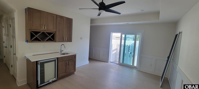 kitchen featuring a sink, a decorative wall, light countertops, light wood-style floors, and wine cooler