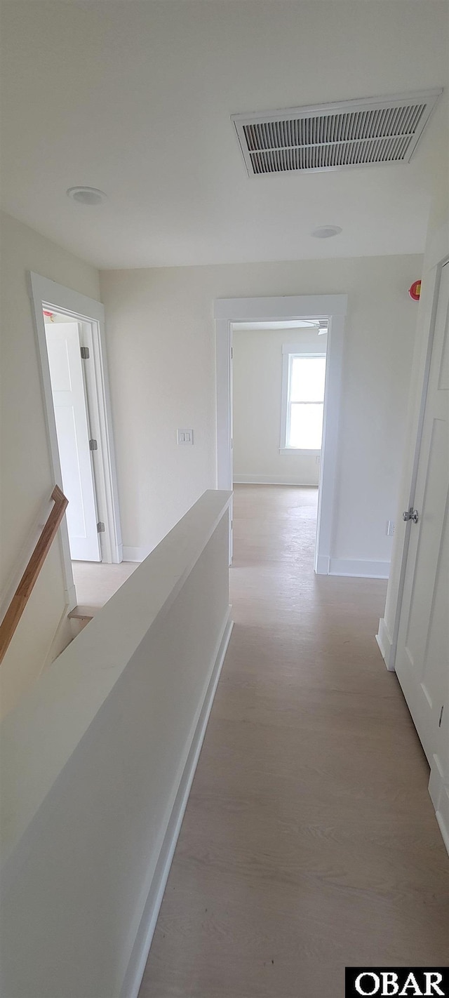 corridor with baseboards, an upstairs landing, light wood-style flooring, and visible vents