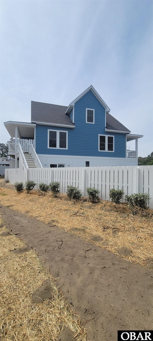 exterior space featuring fence, a shingled roof, and stairs