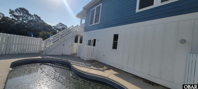 view of side of property with board and batten siding, fence, an outdoor pool, a patio area, and stairway