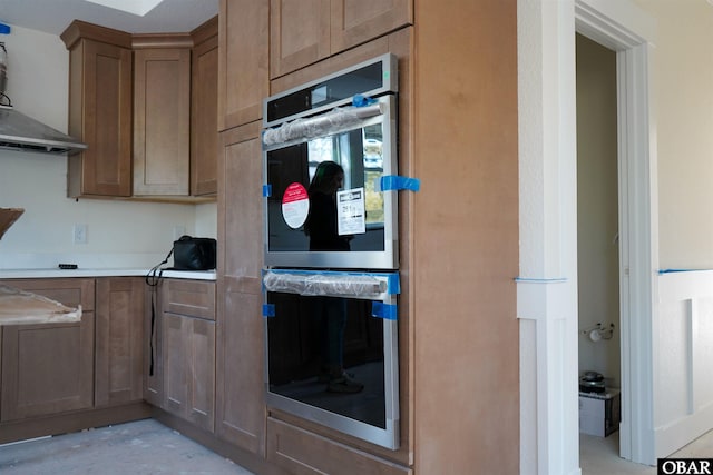 kitchen with light countertops, double oven, and wall chimney exhaust hood
