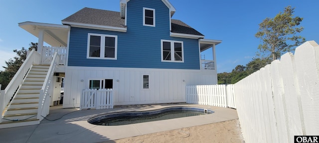 rear view of property featuring an empty pool, a shingled roof, stairway, and a fenced backyard