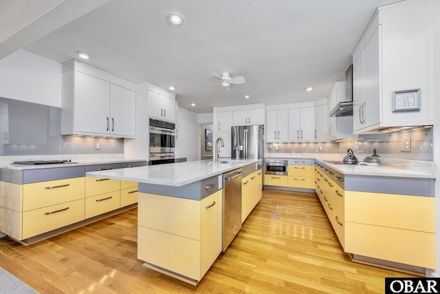 kitchen featuring tasteful backsplash, a kitchen island with sink, stainless steel appliances, light wood-type flooring, and a sink