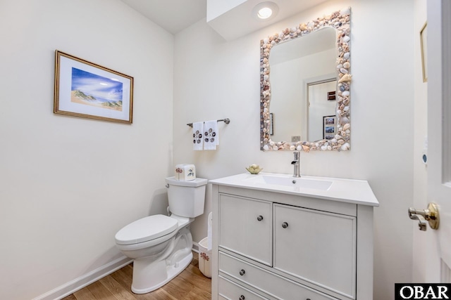 half bathroom featuring wood finished floors, vanity, toilet, and baseboards