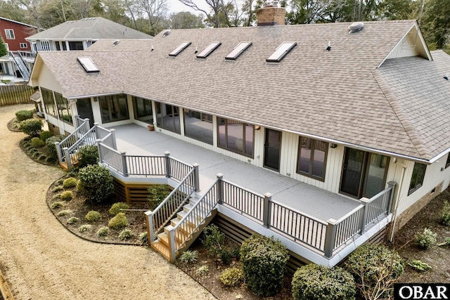 rear view of house with a shingled roof, a sunroom, stairs, a wooden deck, and a chimney