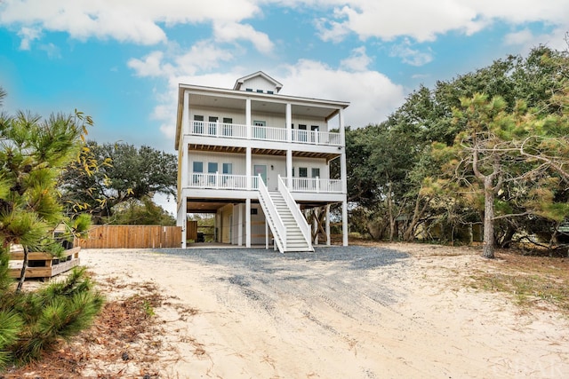 beach home featuring driveway, a balcony, stairs, fence, and a carport