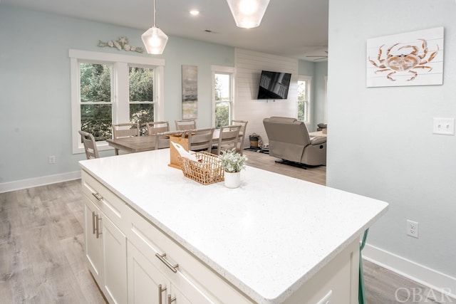 kitchen featuring white cabinets, light wood-style flooring, a kitchen island, open floor plan, and hanging light fixtures