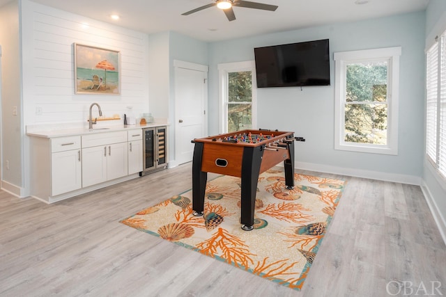 recreation room with light wood-style flooring, a sink, wet bar, beverage cooler, and baseboards