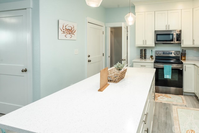 kitchen featuring stainless steel appliances, hanging light fixtures, white cabinetry, light stone countertops, and light wood-type flooring