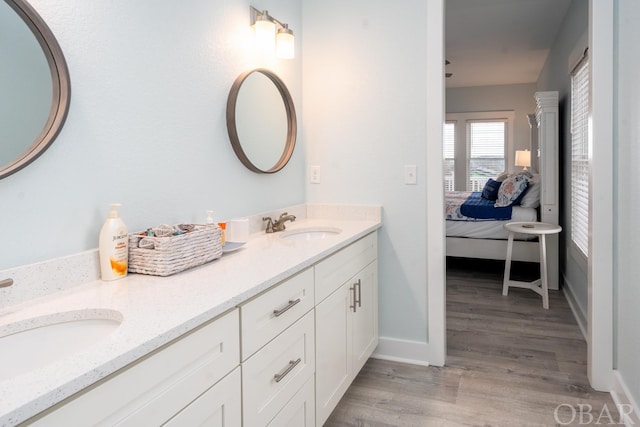 ensuite bathroom featuring double vanity, a sink, ensuite bath, and wood finished floors